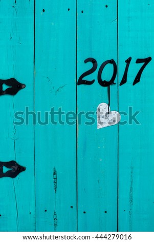 Year 2017 in black iron numbers and tin heart hanging on antique rustic teal blue wooden door; Valentine's Day and love concept with painted copy space