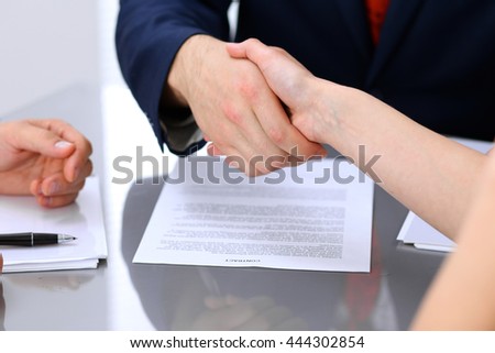 Businessman and business woman shaking hands to each other above signed contract