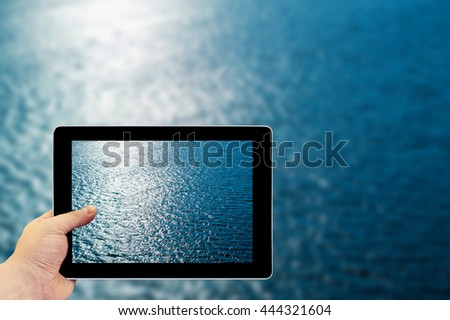 Tablet photography concept. Taking pictures on a tablet. Blue water with sun reflections
