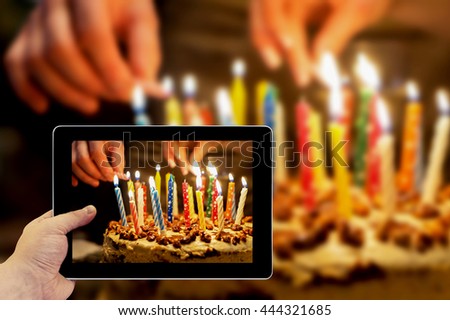 Tablet photography concept. Taking pictures on a tablet. Birthday cake with burning candles in the dark background