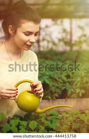 Farmer girl watering green plants in greenhouse. Portrait of cheerful farm worker woman working in hothouse. Organic food farm harvest. BeH3althy concept photo