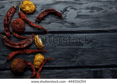 wrinkled dried red chili pepper and apples on dark textured wooden background in round shape, copy space
