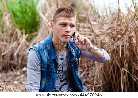 young handsome stylish hipster man looking for something in his smartphone, social networking, apps, search, sms, speaking phone, outdoors nature yellow and green