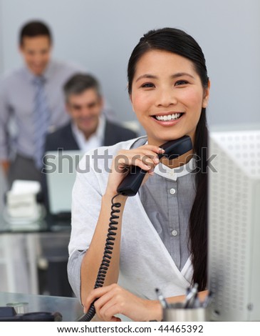 Confident asian businesswoman at her desk with her colleagues in the background