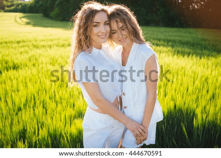 curly sisters twins hugging on wheat sunny field. Family happiness and understanding. Happy Friends walk in sunny weather outdoors.
