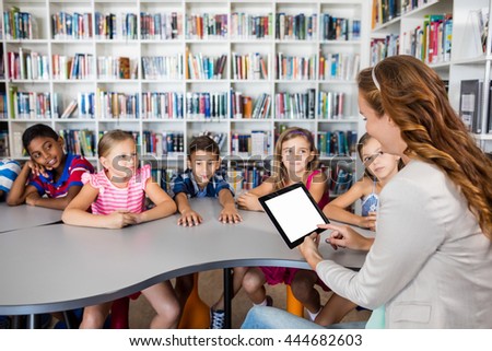 Teacher using tablet with pupils in library