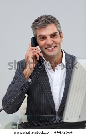 Smiling mature male executive talking on phone at his desk