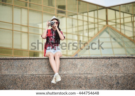 Girl tourist taking pictures of the urban landscape, sitting on a marble surface against the building with a glass facade
