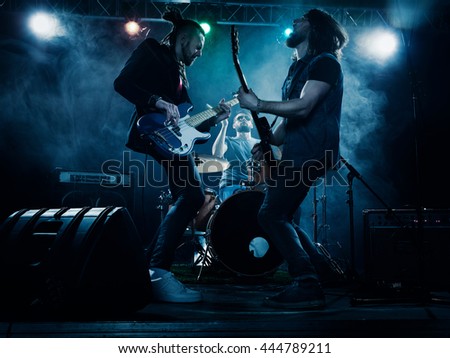 Rock band performs on stage. Guitarist, bass guitar and drums. The guitarist plays solo. Royalty-Free Stock Photo #444789211