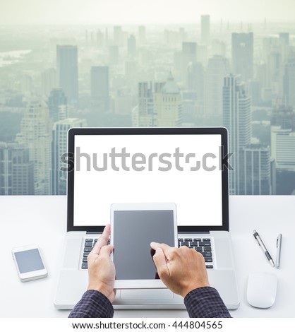 Hand holding tablet computer and laptop computer  on office table with skyline background