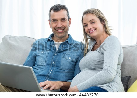 Portrait of couple sitting together on sofa and using laptop