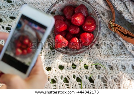 Young hipster girl taking a photo of her lunch food outdoors, chick photographing her strawberry in plate for her  page on her white cell phone, modern young healthy lifestyle concept 