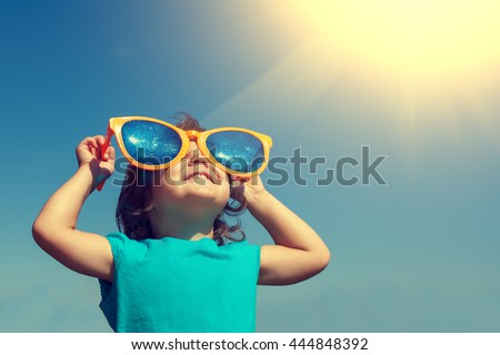 Happy little girl with big sunglasses  looking at the sun Royalty-Free Stock Photo #444848392