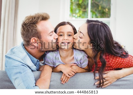 Mother and father kissing daughter while leaning on sofa at home
