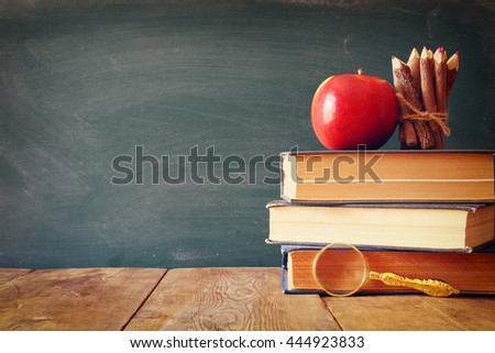 Back to school concept. Blackboard with books, pencils and apple on wooden desk. vintage filtered