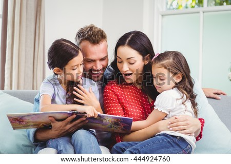 Happy family looking in picture book while sitting on sofa in living room