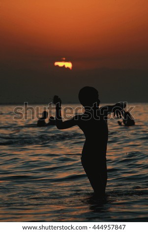 Silhouette a happy little boy playing in sea at sunset