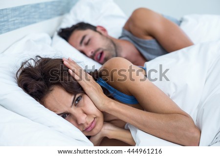 Portrait of woman blocking ears with hands while man snoring on bed Royalty-Free Stock Photo #444961216