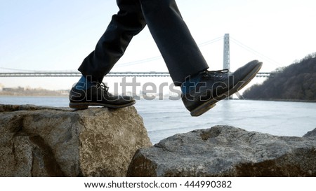 close up of feet walking step by step overcoming obstacles moving into bright future success. one person climbing over rock stones crossing river. bridge landscape background  