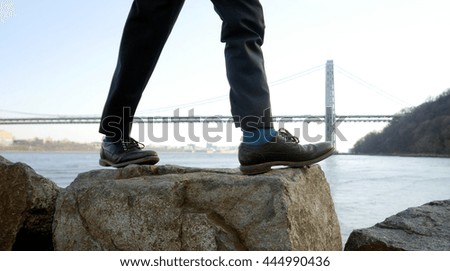close up of feet walking step by step overcoming obstacles moving into bright future success. one person climbing over rock stones crossing river. bridge landscape background  