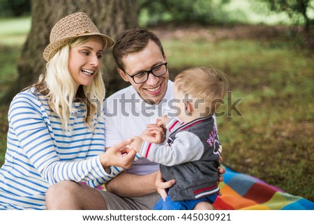 Beautiful young family with a small boy in checkered blankets resting in the park with wicker basket filled with food and drink. Following, fun, pictures