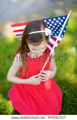 Adorable little girl holding american flag outdoors on beautiful summer day. Independence Day concept.