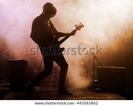 Rock band performs on stage. Guitarist, bass guitar and drums. The guitarist plays solo. Royalty-Free Stock Photo #445065862