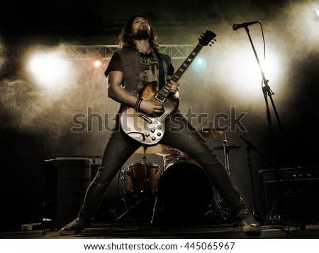 Rock band performs on stage. Guitarist, bass guitar and drums. The guitarist plays solo. Royalty-Free Stock Photo #445065967