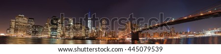 New York City Manhattan skyline panorama with Brooklyn Bridge and office skyscrapers building in at dusk illuminated with lights at night.