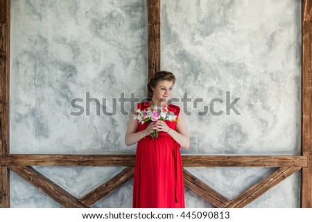 Beautiful charming stylish pregnant woman close-up portrait in a long red dress smart with a bouquet of roses and peony in hands standing near the wall textured background look not at the camera