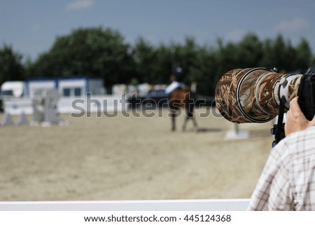 Huge zoom lens on a camera, professional photographer taking a picture by zoom lens at a show jumping competitions, camera lens in focus 
