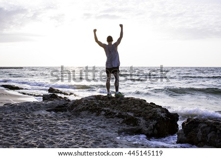 Young sporty male with rised hand watching sunrise in the sea