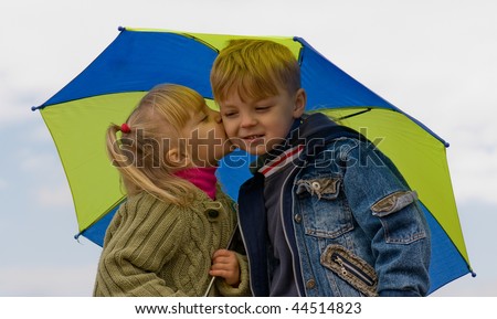 Little girl kiss boy, under umbrella in autumn day