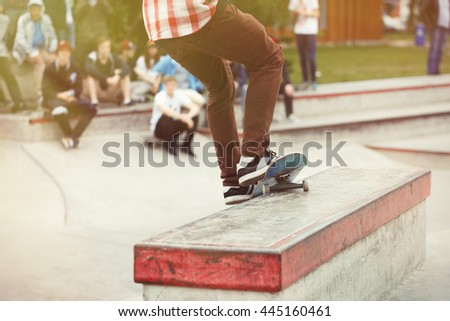 Skater grinds on ledge with skateboard. Skateboarder performs smith grind trick on skate contest in concrete skatepark. Extreme summer sports activity. Teenager boy doing tricks on skate board