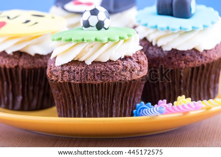 Delicious cupcakes with icons of ball, tuxedo, smiley and camera on it with yellow plate and three candles on wooden desk and blue background