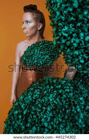 Studio fashion portrait of a young beautiful woman with creative make up wearing bronze dress stay for tree