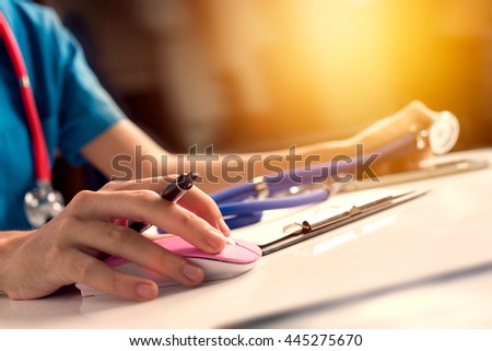 Close up asian woman doctor working in hospital using computer mouse and holding stethoscope to check for virtual patient, vintage tone with sunlight effect picture.