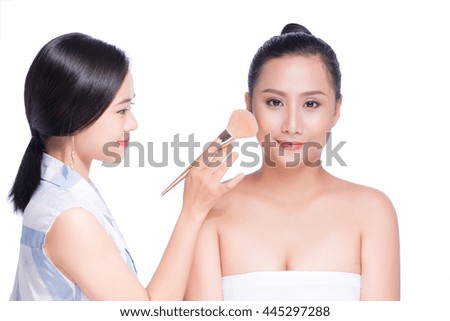 Make-up artist applying powder with a brush on model's cheeks of asian young woman with big beautiful eyes on white background