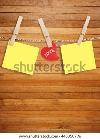 Blank yellow of paper with wood clip on wood background design, decorated red heart concept.
