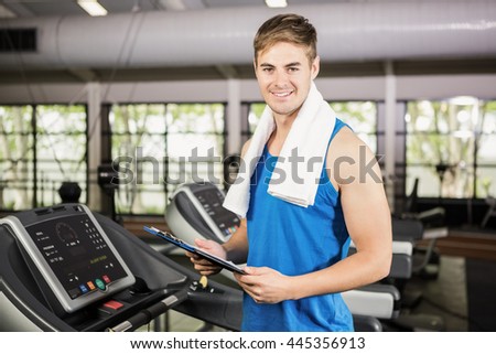 Portrait of trainer holding clipboard on treadmill at gym