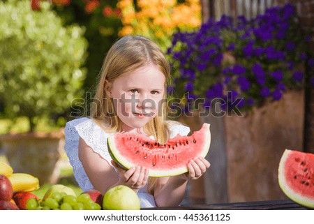 Happy girl with big red slice of watermelon sitting on rustic tabels in summer garden.
