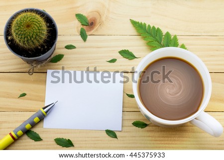 Coffee mug with green foot fern, Flower petals, Cactus flower, Pen and notes on yellow rustic table.