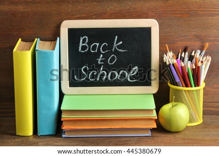wooden plaque with the inscription "back to school" near the pencil box with school equipment and Apple with stack of books and notebooks on brown wooden background  Royalty-Free Stock Photo #445380679
