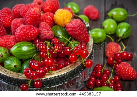 Mix of fresh organic garden berries raspberry, currants, gooseberries, cloudberry on wooden table background closeup