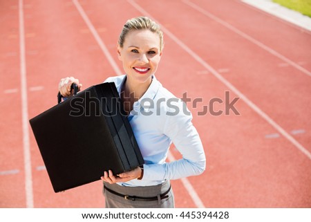 Portrait of happy businesswoman standing on running track with briefcase
