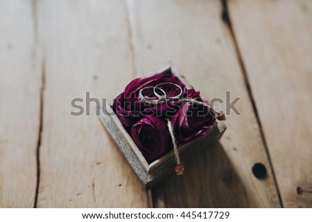 Wedding rings of the bride and groom are in a box with red flowers on a wooden table