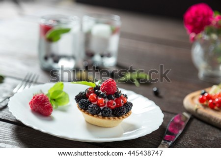 Delicious berry cake on a white plate. Served with lemonade, ice, mint and flowers on wooden table. Silver knife and fork. Horizontal image.