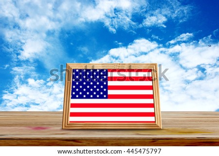 American flag in wooden frame on wooden table, blue background