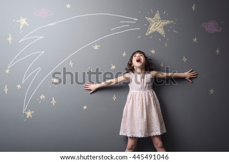 Little girl screams from pleasure to see a shooting star, the grace of the space and big planet depicted with chalk on the grey wall in studio. True emotion of happiness.