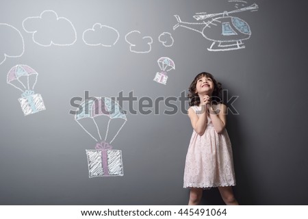 Dreams come true for the baby. Little girl is happy to receive presents on parachutes from the helicopter depicted with chalk on the neutral background.